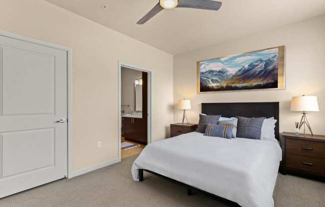 View into the cozy bedroom with a large bed, two side tables, and a ceiling fan with access into the bathroom at Sylvan Uptown, Denver