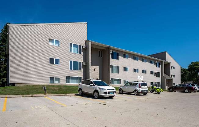 A grey building with a parking lot in front of it. Bismarck, ND Bradbury Apartments