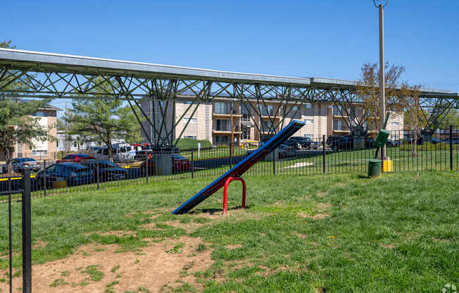 A playground with a red and blue slide and a metal structure in the background.