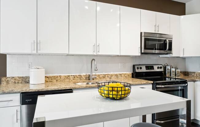 a kitchen with white cabinets and a white island with a bowl of lemons on it