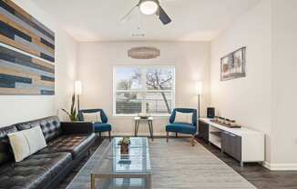 A living room with a black leather couch, a glass coffee table, and a ceiling fan.