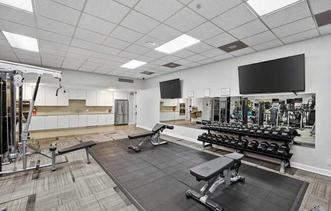 A gym with a variety of equipment including a bench press, a squat rack, and a television.