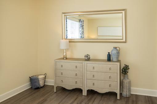 A large mirror hangs over a white dresser with a lamp and vases on top.