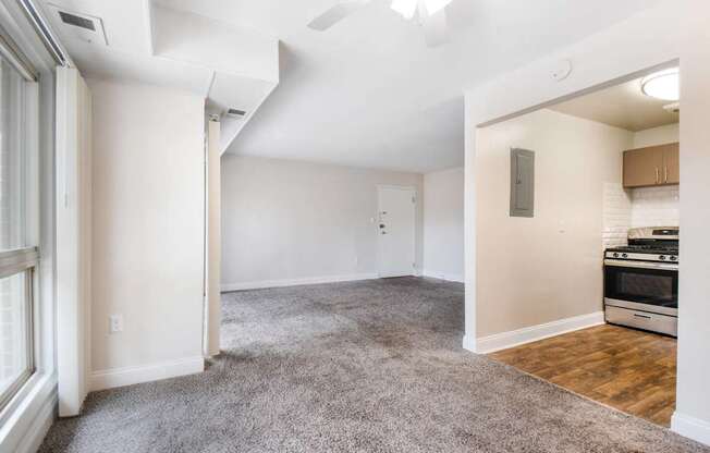 A spacious living room with a grey carpet and a kitchen area with a stove and oven.
