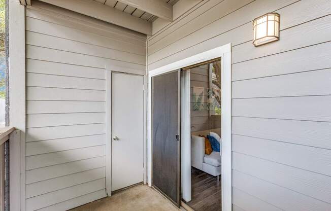 A white door with a glass window is open to a room with a couch and a lamp.