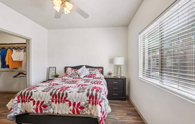 A bedroom with a bed, nightstand, and a window with blinds.