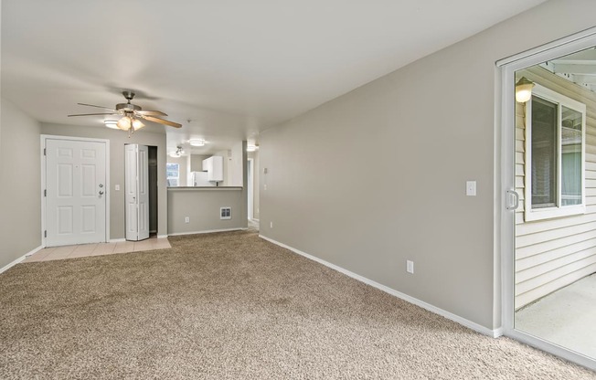 an empty living room with a ceiling fan and a door to a kitchen