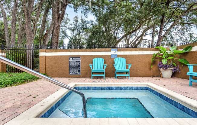 a swimming pool with two chairs and a hot tub in a yard with a fence