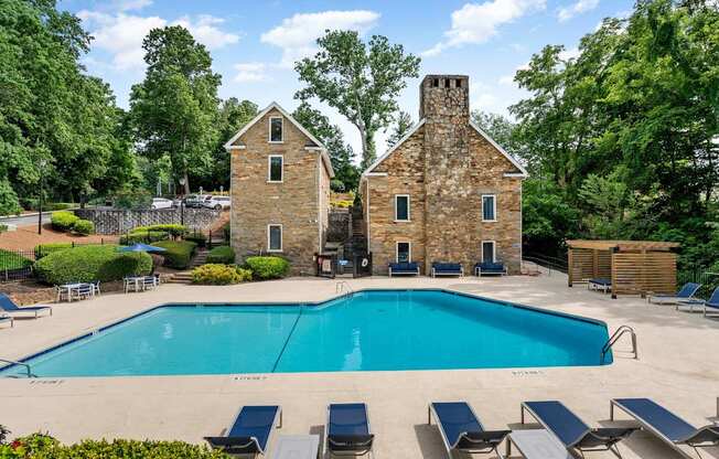 A large swimming pool surrounded by lounge chairs and two stone buildings. at Mill House at East Cobb, Marietta, 30067