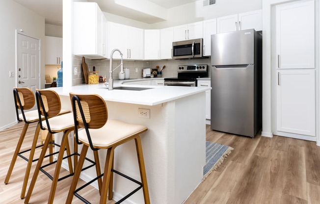 a kitchen with a large island with stools and a stainless steel refrigerator