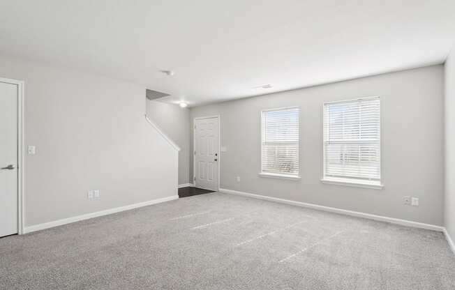 A spacious room with a carpeted floor and a staircase leading to another room.