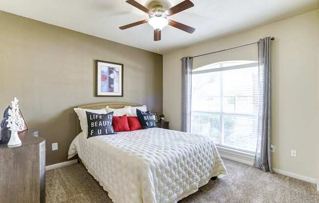 A bedroom with a bed, pillows, a ceiling fan, and a window with curtains.