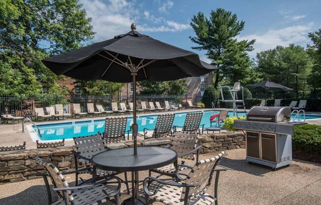 A black umbrella shades a table in a backyard with a pool.