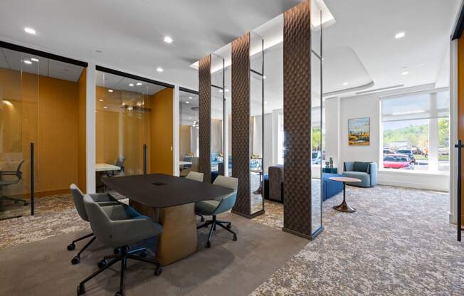 Meeting rooms with tables and chairs near a community lounge with comfortable seating and large windows.