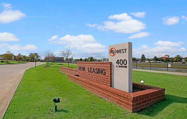 Sign advertising leasing at "49 West, 400 S. Dodson." The sign is on a brick base, surrounded by neatly mowed grass, with a clear sky above.