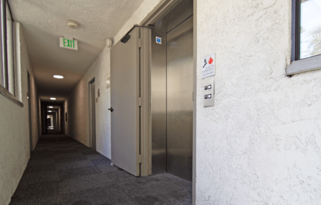 A long hallway with a metal exit sign on the ceiling.