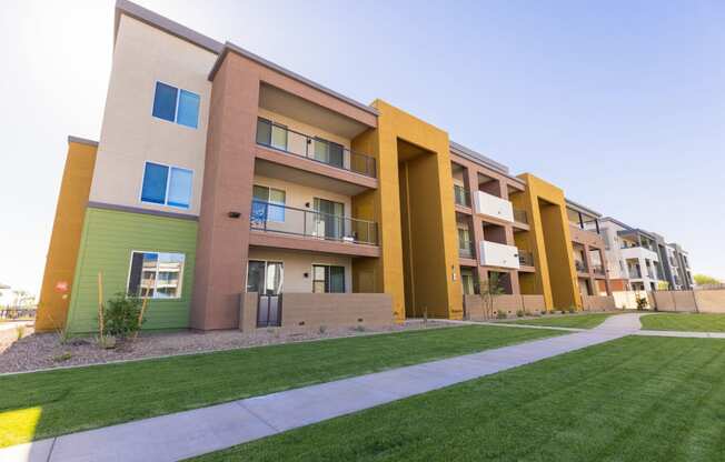 an exterior view of an apartment complex with green grass and a sidewalk