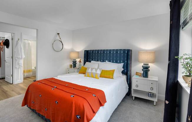 A bedroom with a white bed and orange bedspread.
