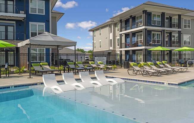 a swimming pool with lounge chairs and umbrellas in front of apartment buildings