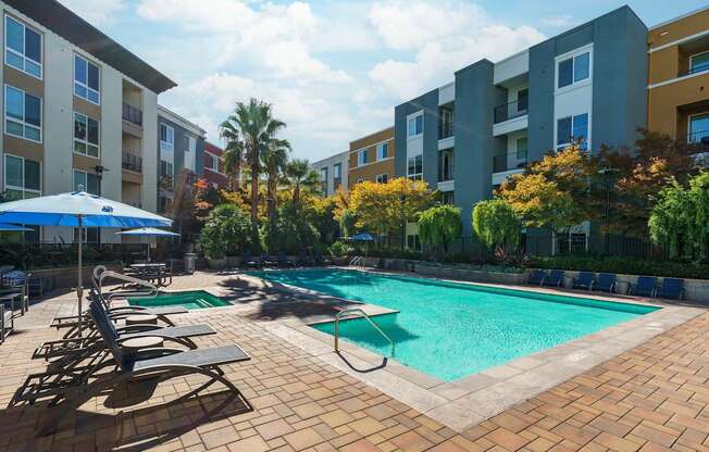 A swimming pool surrounded by lounge chairs and umbrellas in a residential area.