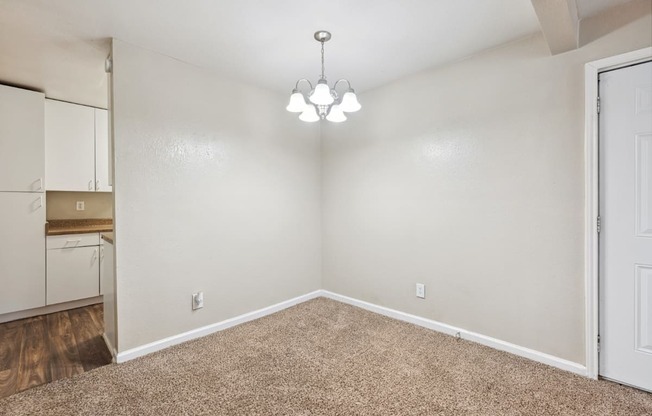 the spacious living room with white walls and carpet and a door to the kitchen