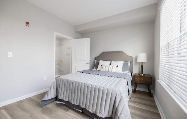A bedroom with a bed, nightstand, and window with blinds at Harbor Pointe Apartments, New Jersey, 07002