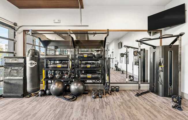 A gym with a variety of equipment including a squat rack, weight bench, and a television mounted on the wall.