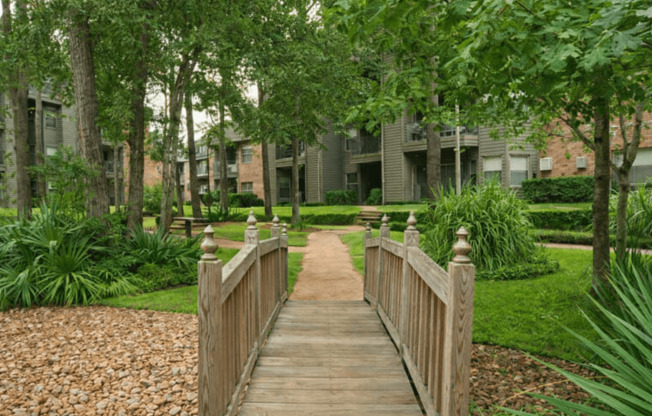 A wooden bridge leads to a building in a green landscape.