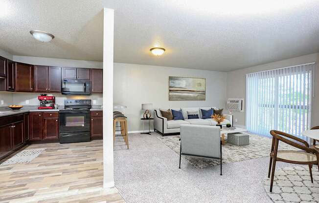 A living room with a grey couch and a kitchen area with brown cabinets.
