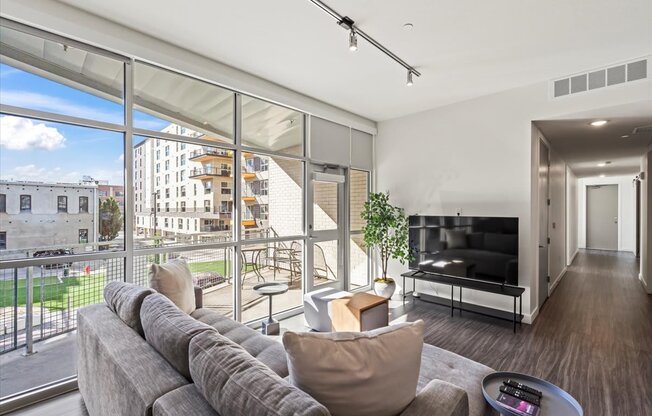 A modern living room with a grey sofa and a large window overlooking a cityscape.