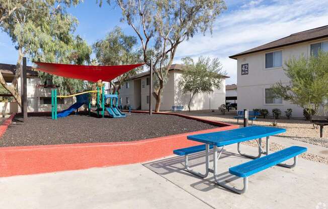 A playground with a red shade sail and blue benches.