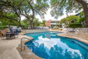 A swimming pool surrounded by trees and chairs.