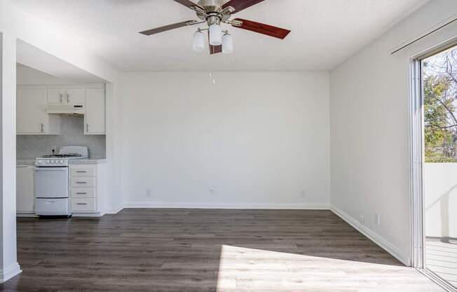 an empty living room with a ceiling fan and a kitchen