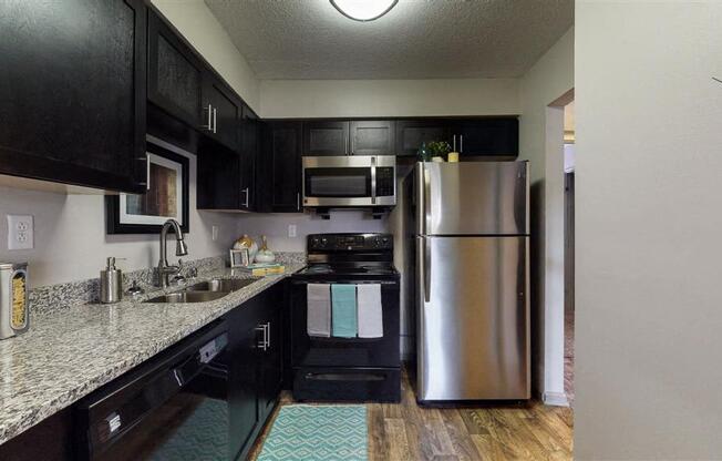 A kitchen with black cabinets and a stainless steel refrigerator.