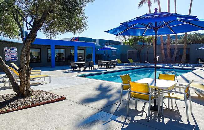 A pool area with a blue umbrella and yellow chairs.