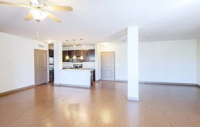 an empty living room with a ceiling fan and a kitchen in the background