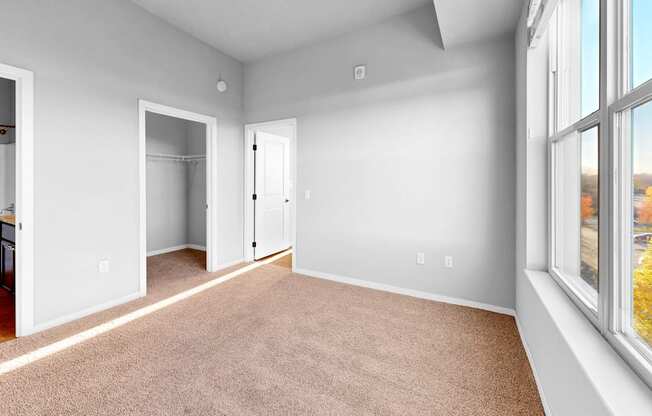 A large, empty room with a carpeted floor and a view of trees outside the window.