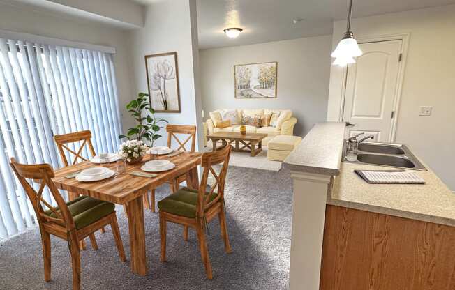 Liberty Landing Apartments in West Jordan Utah living room in Lambert floor plan with four-seat dining table in front of sink and living room in the background.