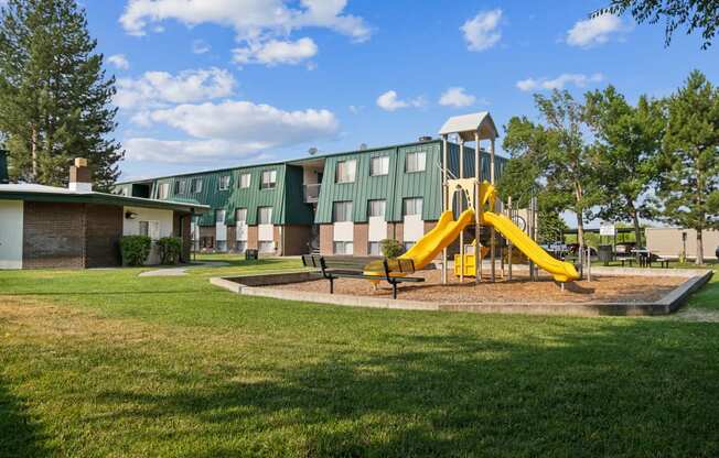 a playground with a yellow swing set in front of a building