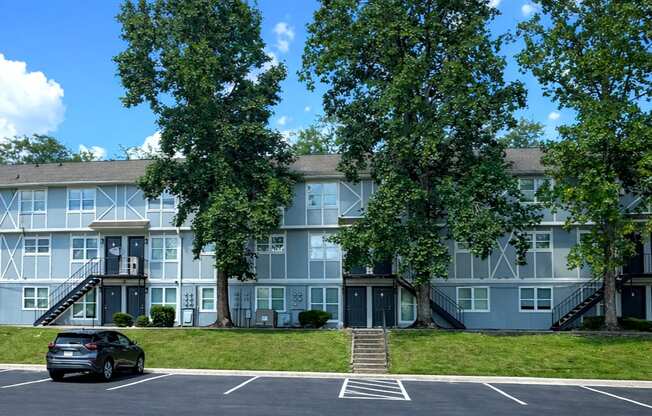A car is parked in a parking lot in front of a building with a tree in front of it.