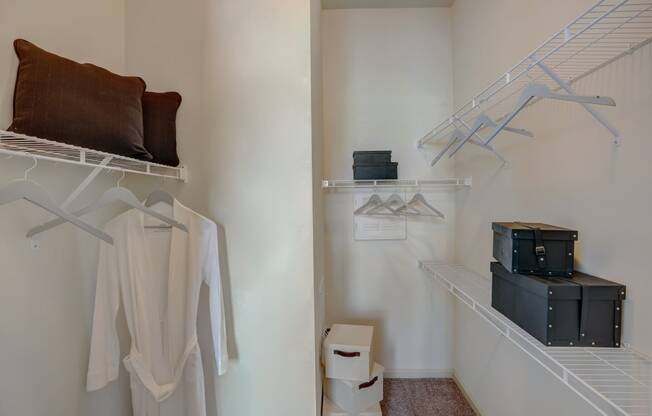 a closet with white clothes and boxes on the floor and a white wall with shelves