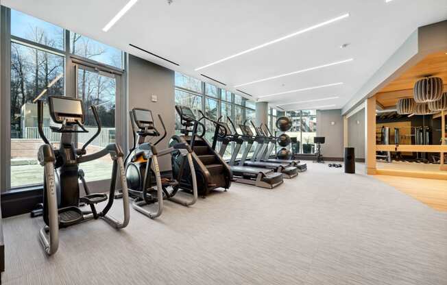 a gym with a row of cardio machines and large windows