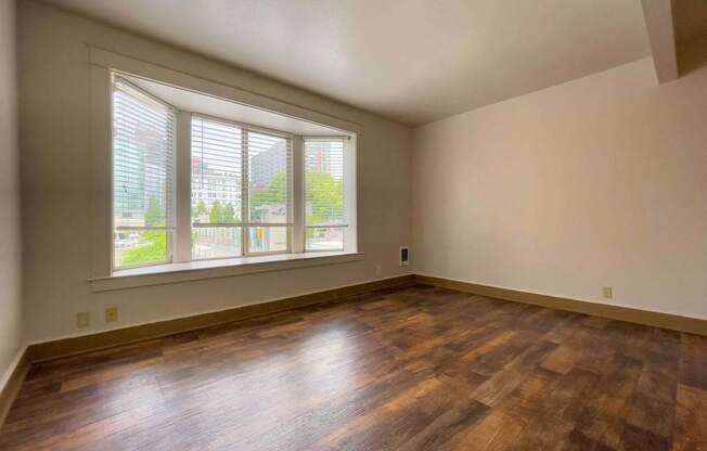 A room with wooden floors and a large window with blinds.