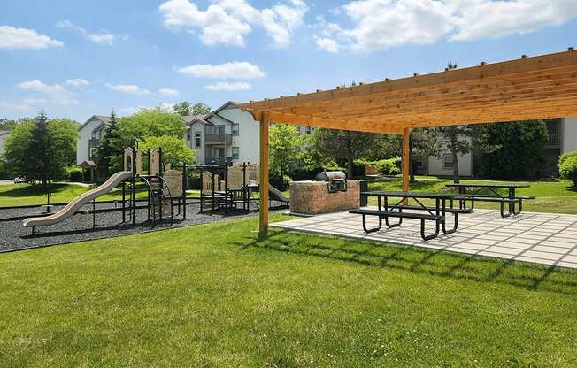 A playground with a slide, swings, and picnic tables under a wooden canopy.
