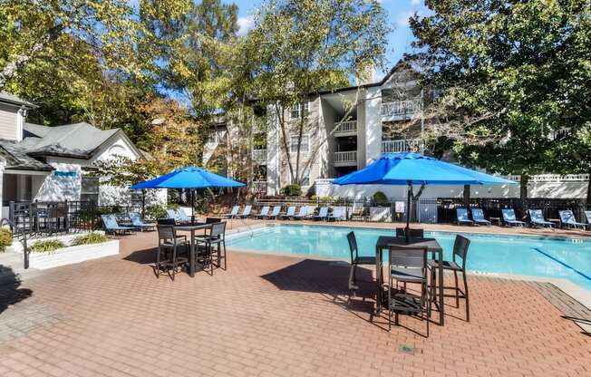 A pool area with chairs and umbrellas is surrounded by trees.