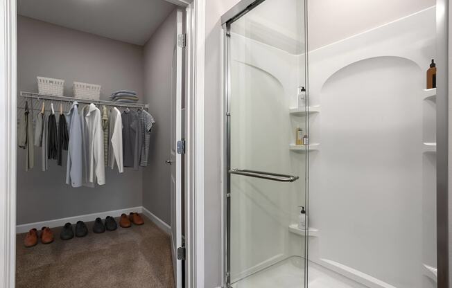 a walk in closet with a glass shower and some clothes on a rack