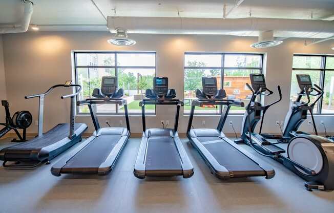 a gym with four treadmills and three windows