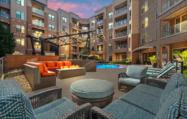 A large outdoor seating area with wicker chairs and tables is surrounded by apartment buildings.