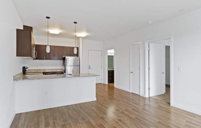 an empty living room with a kitchen and a door to a hallway