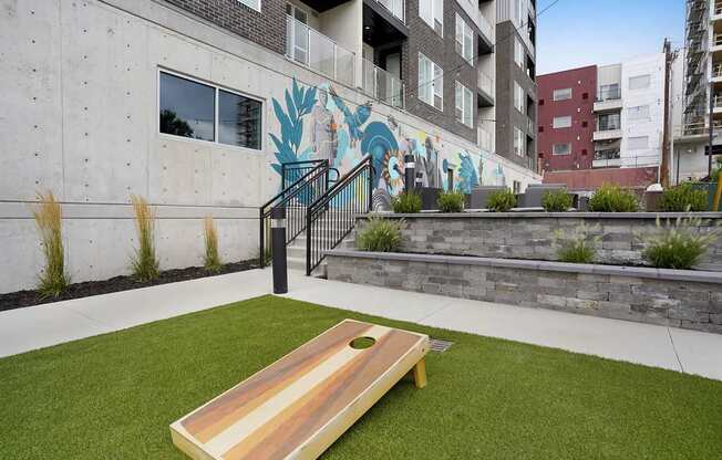 A wooden bench sits on a green lawn in front of a building with a mural.